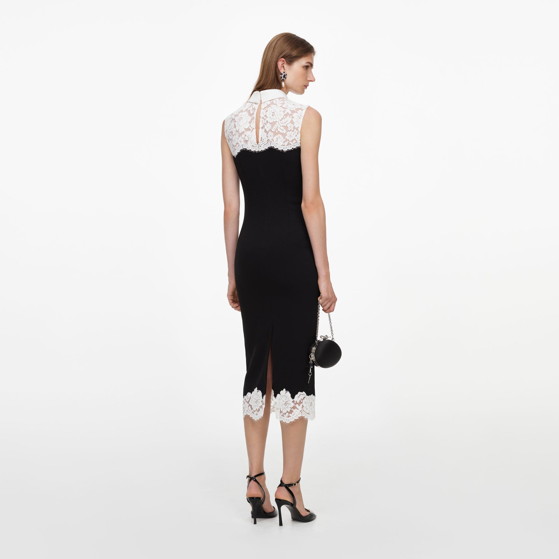 Woman in black and white lace dress, black heels, and round black handbag, viewed from behind