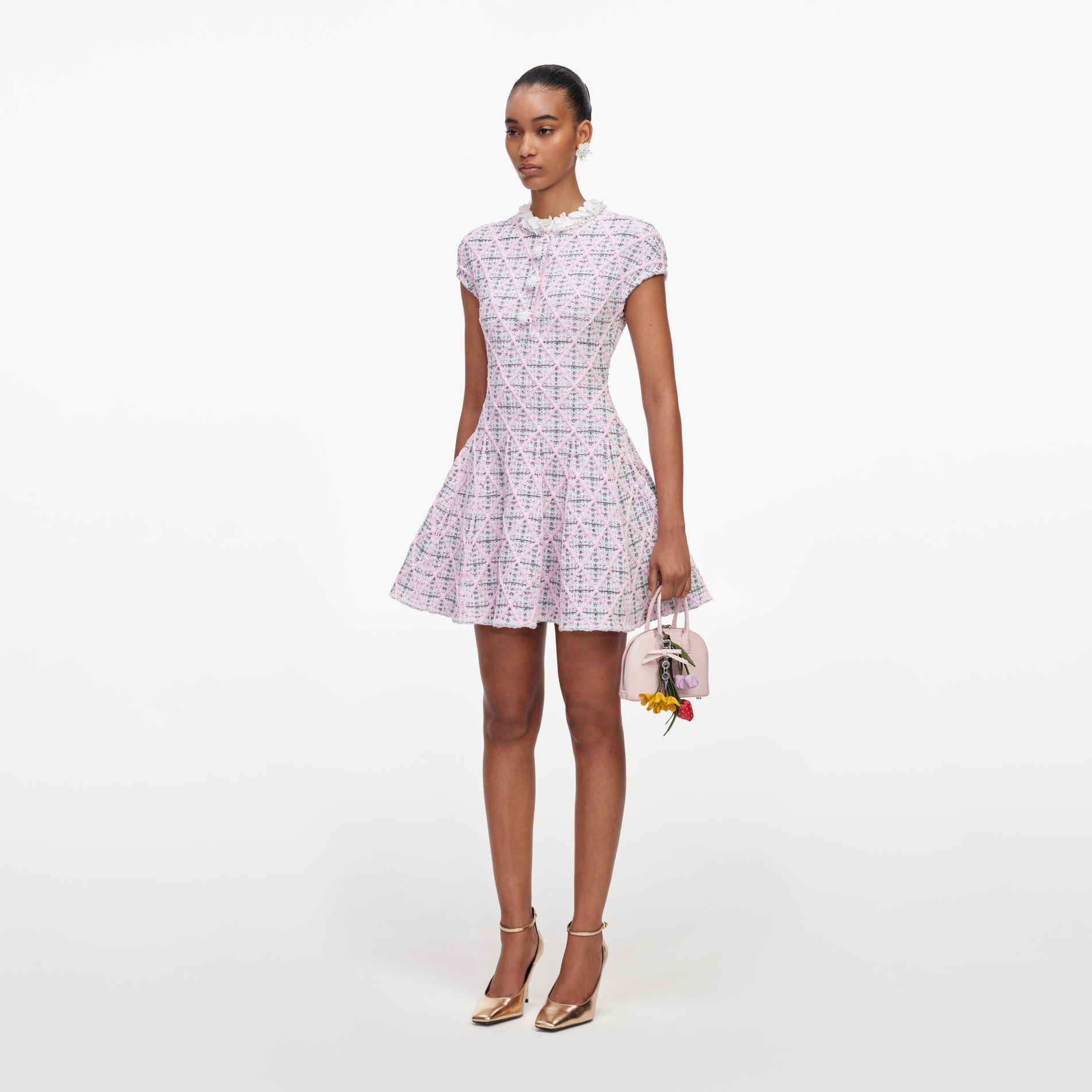 Woman in a pink tweed dress with a ruffled collar, holding a small pink handbag with flower charms