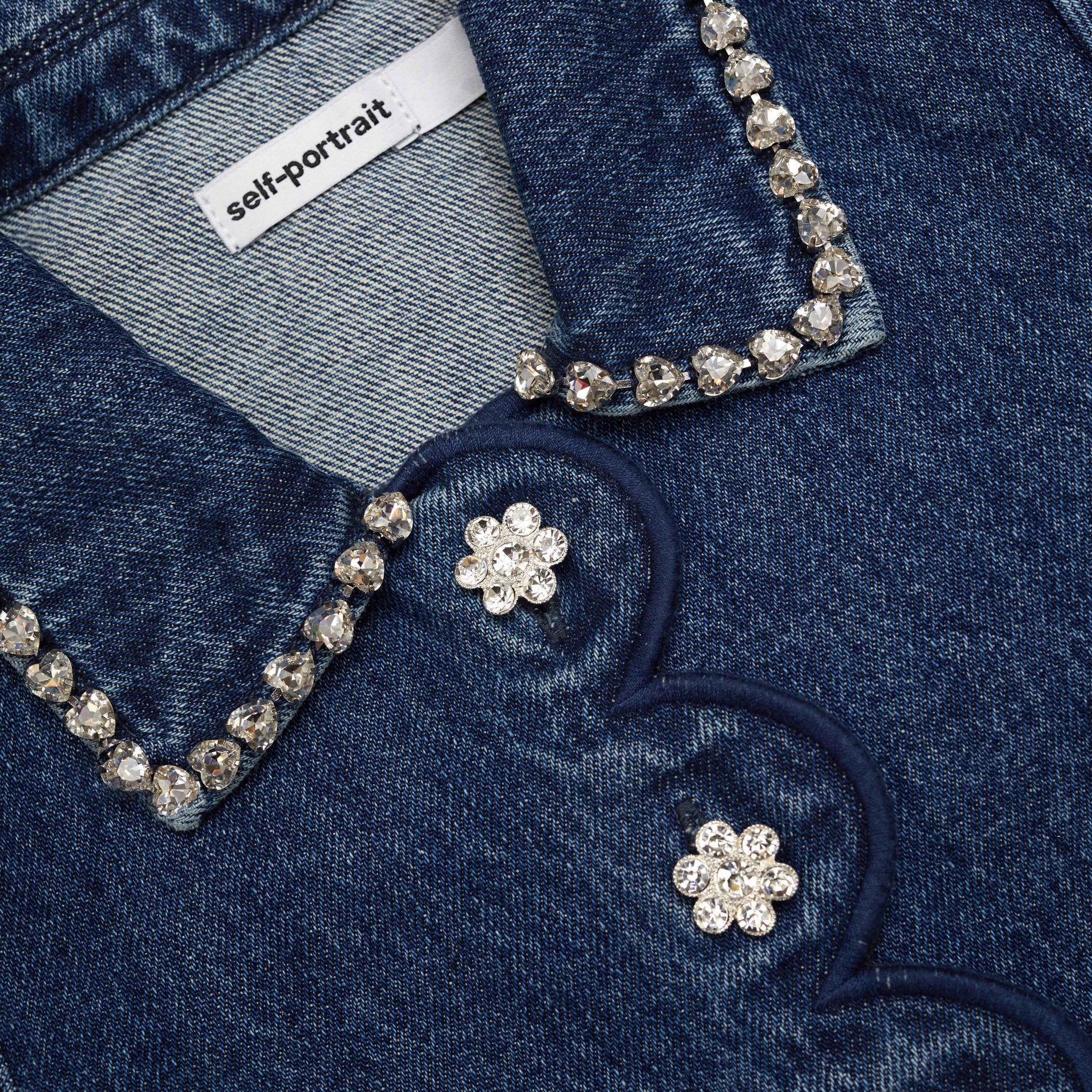 Close up of a Self-Portrait denim shirt with crystal embellishments and flower-shaped buttons
