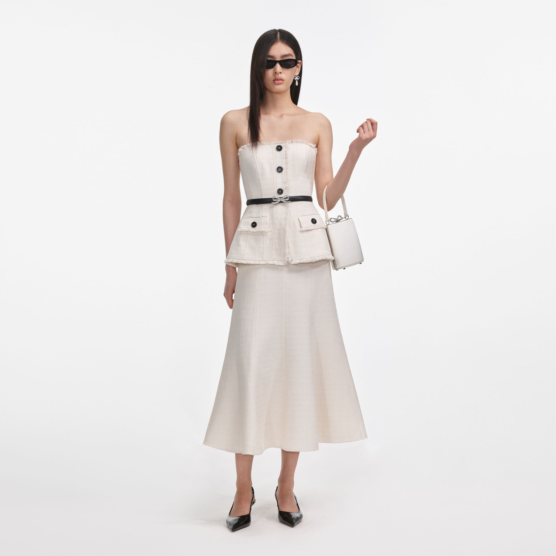 Woman in a white tweed strapless top with black buttons, a black belt with a bow, and a matching white skirt