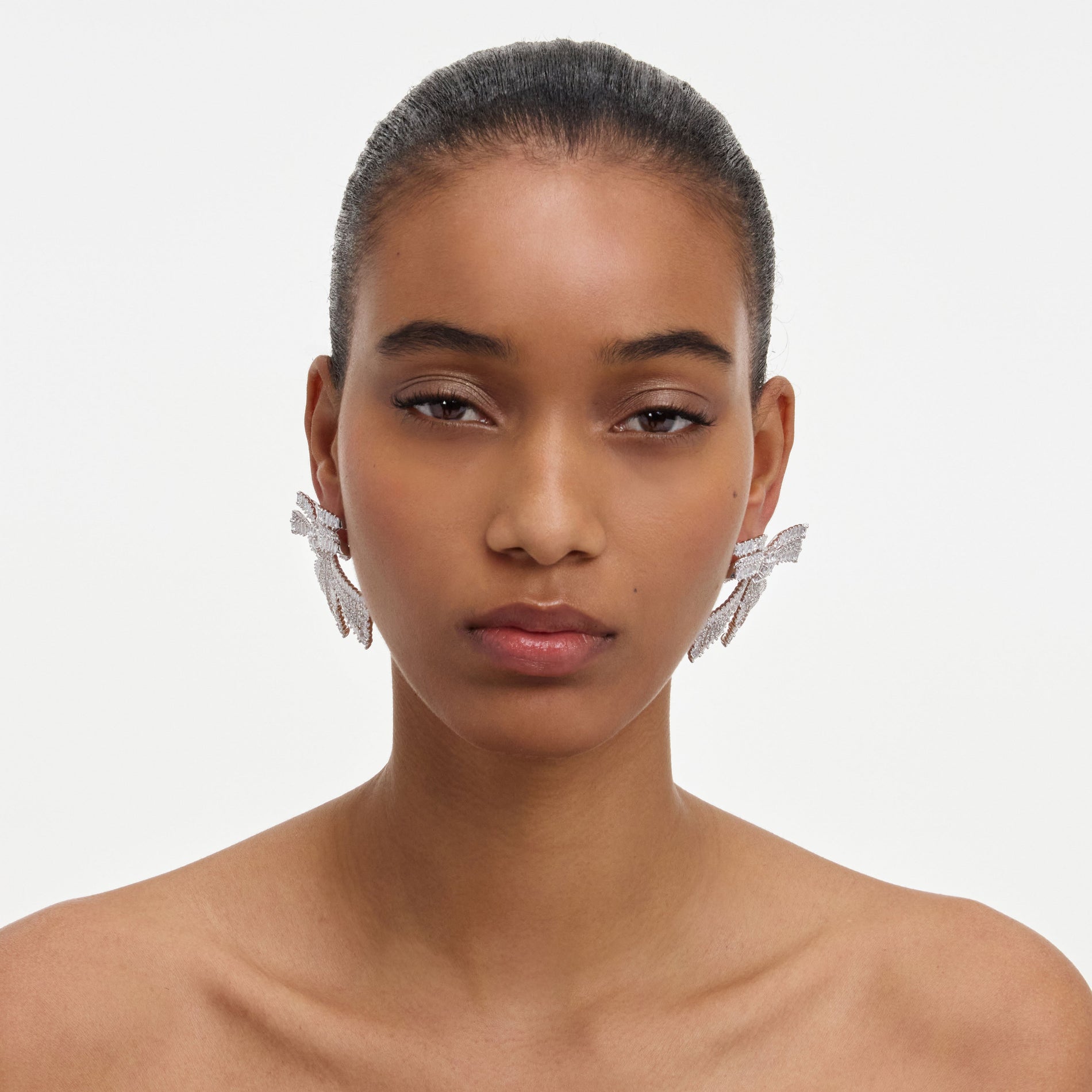A close up of a woman wearing the Crystal Bow Earrings