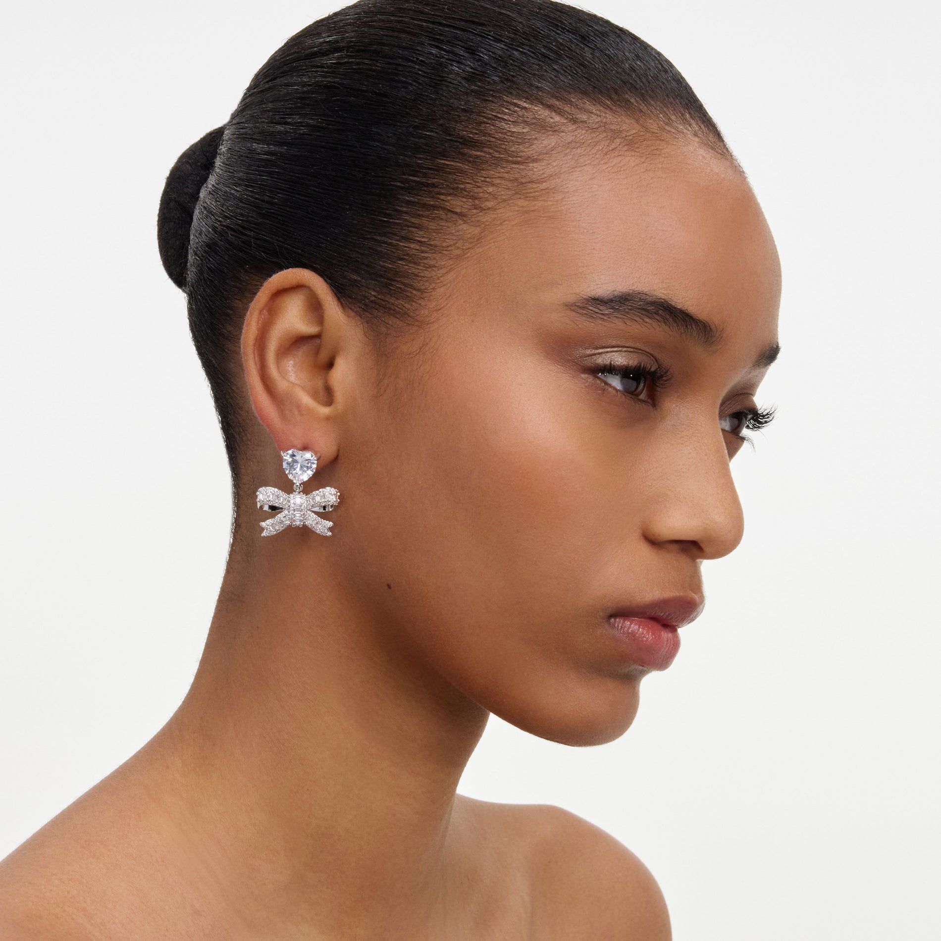 A close up of a woman wearing the Crystal Heart Bow Drop Earrings