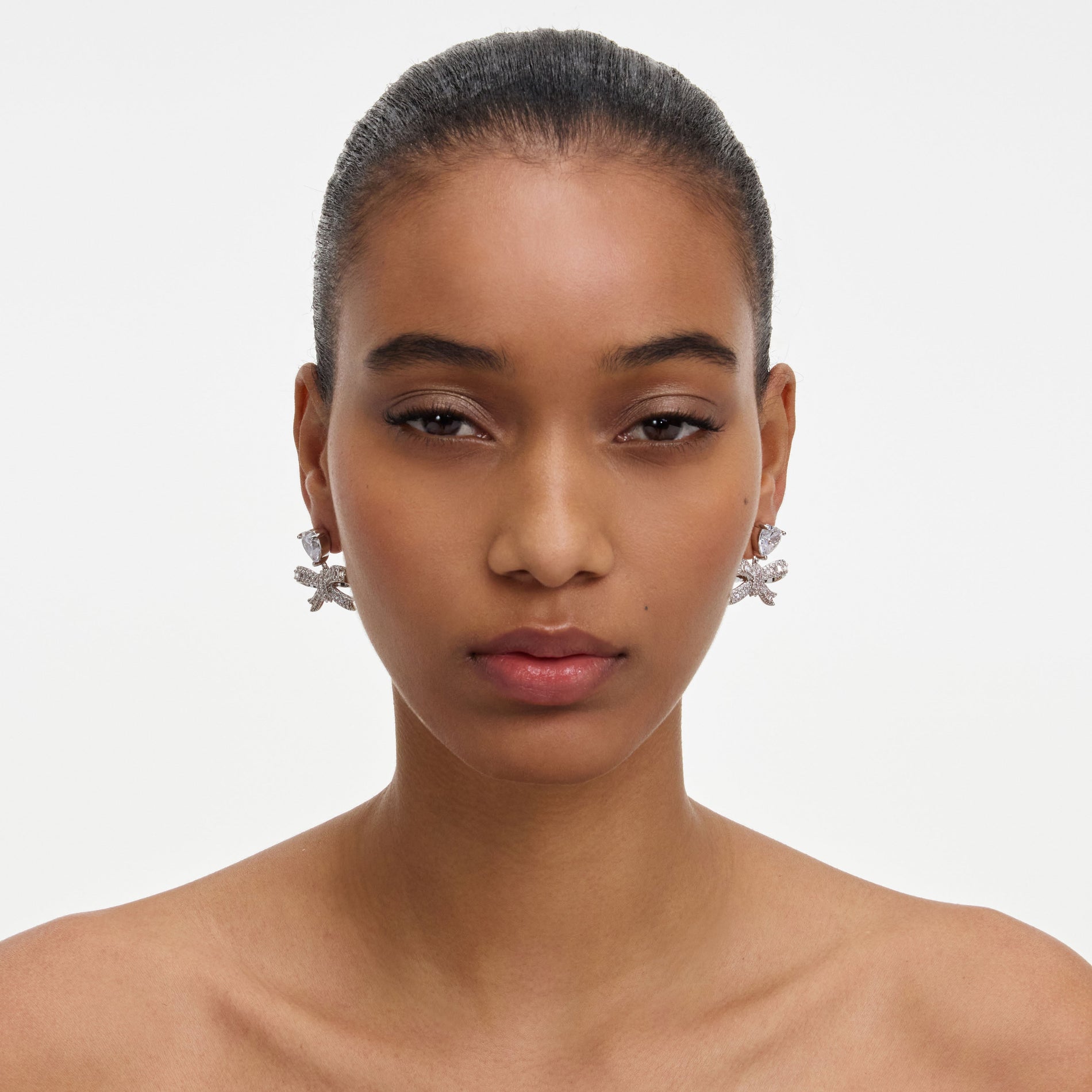 A close up of a woman wearing the Crystal Heart Bow Drop Earrings