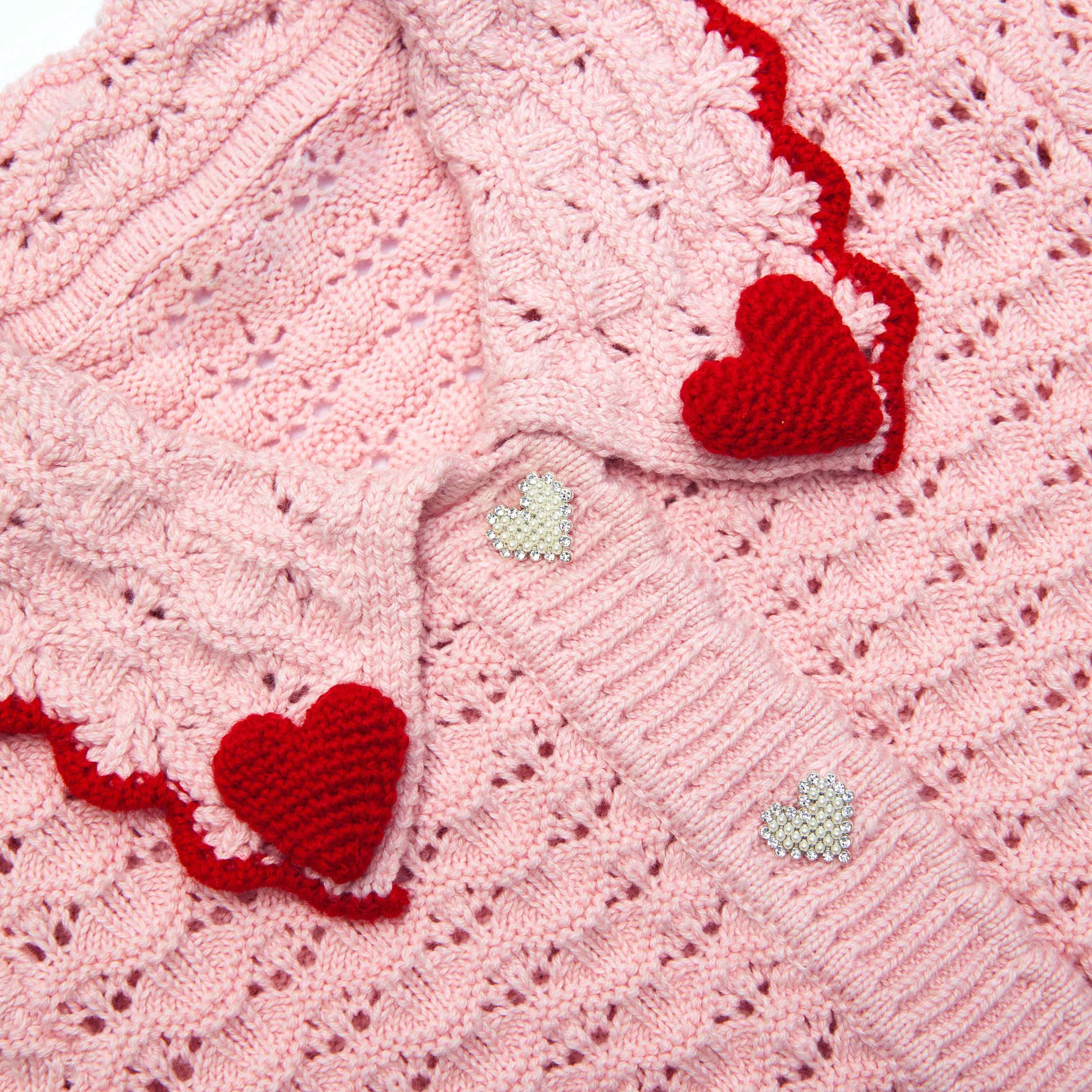 Pink knitted cardigan with red crochet heart details and pearl heart buttons