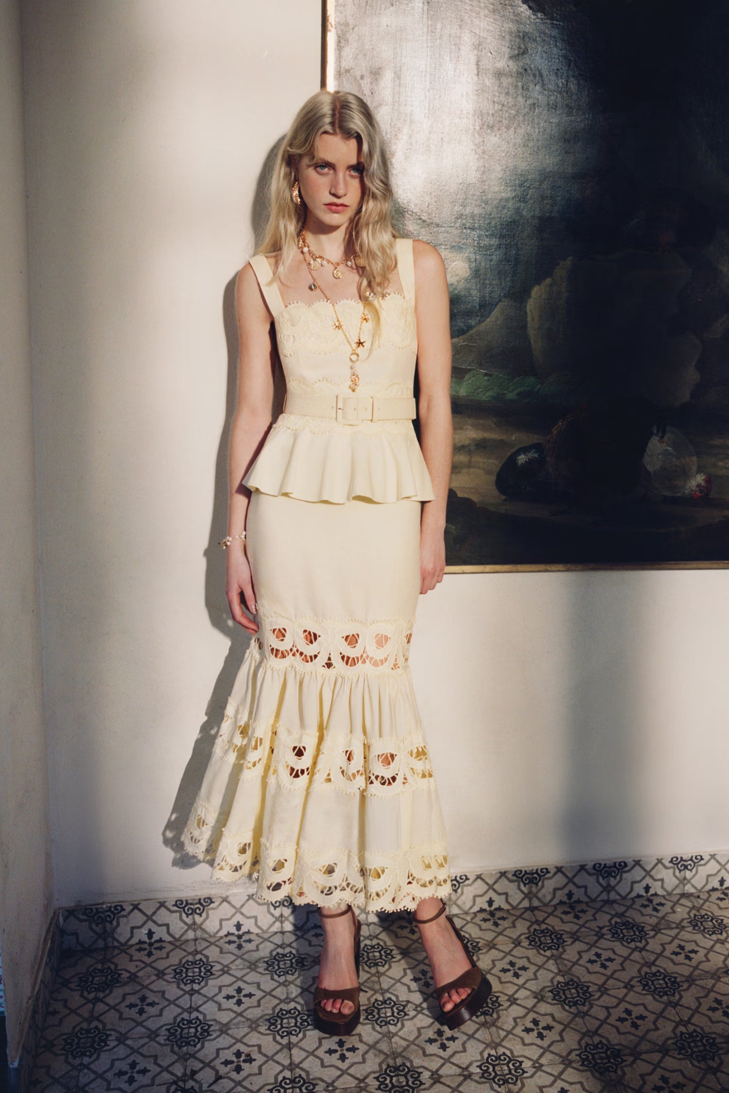 Woman in a yellow lace insert dress standing in a room with a painting on the wall.