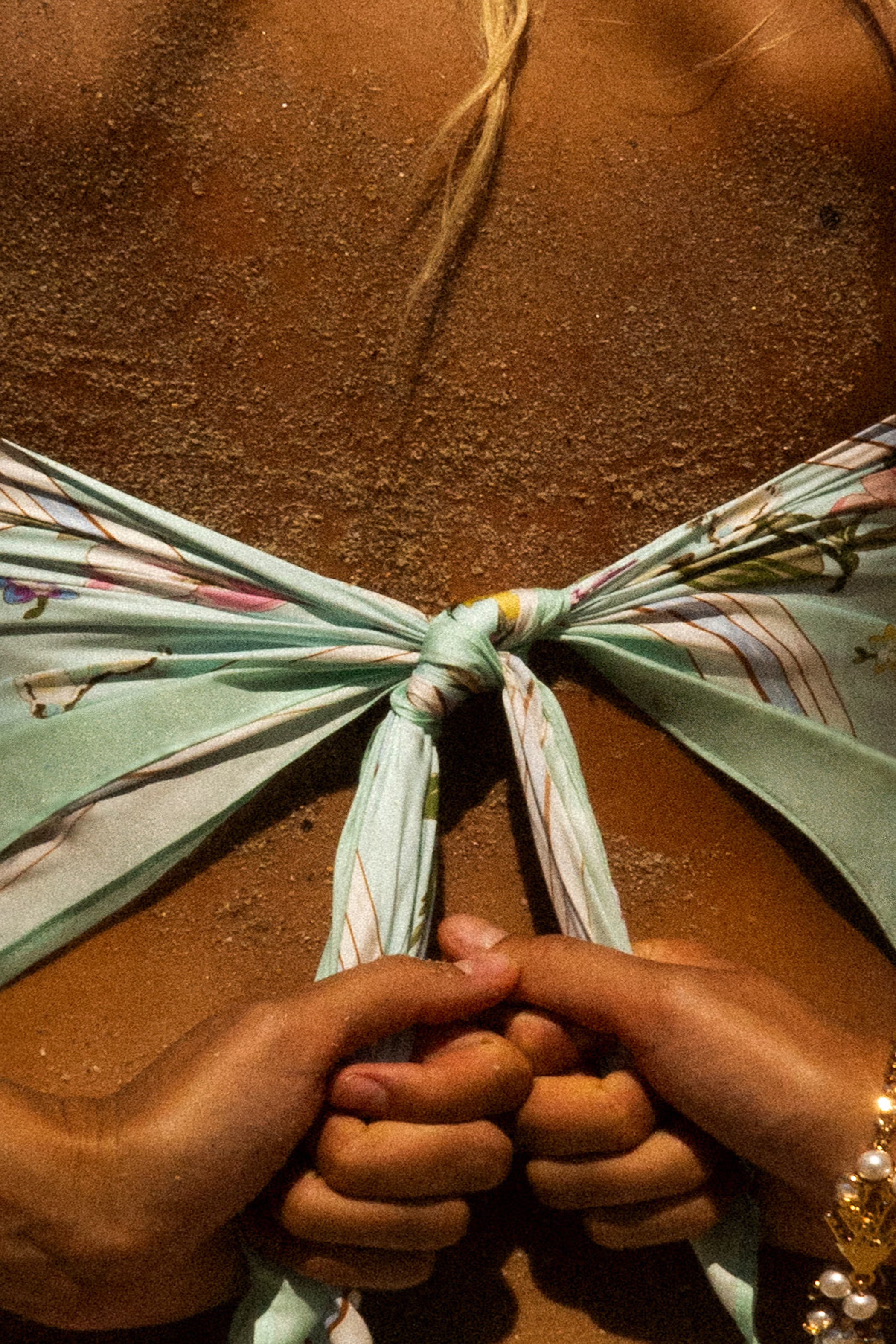 Close-up of hands tying a floral mint scarf.