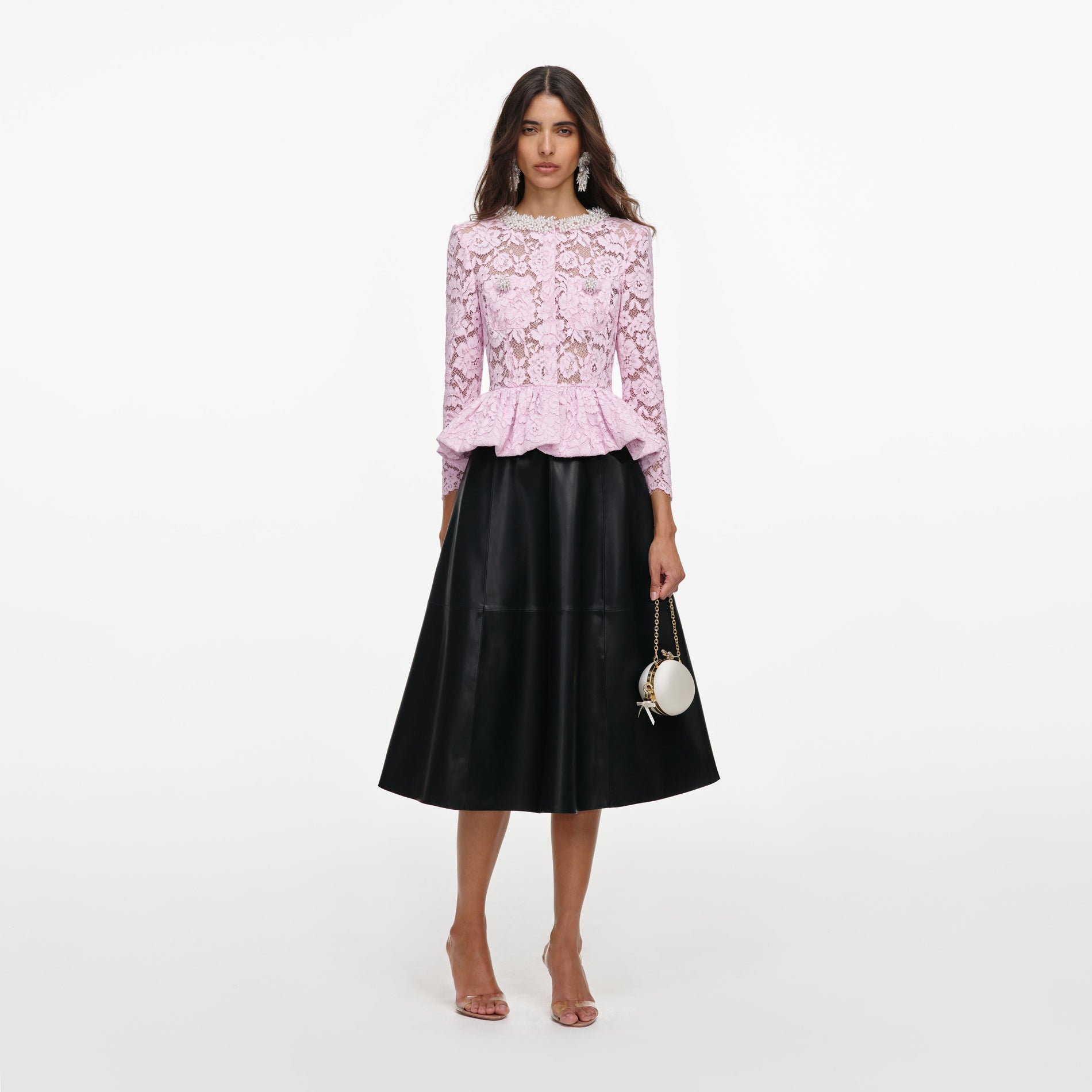 Woman in a pink lace top with a pearl collar, a black leather skirt, clear heels, and a white round handbag
