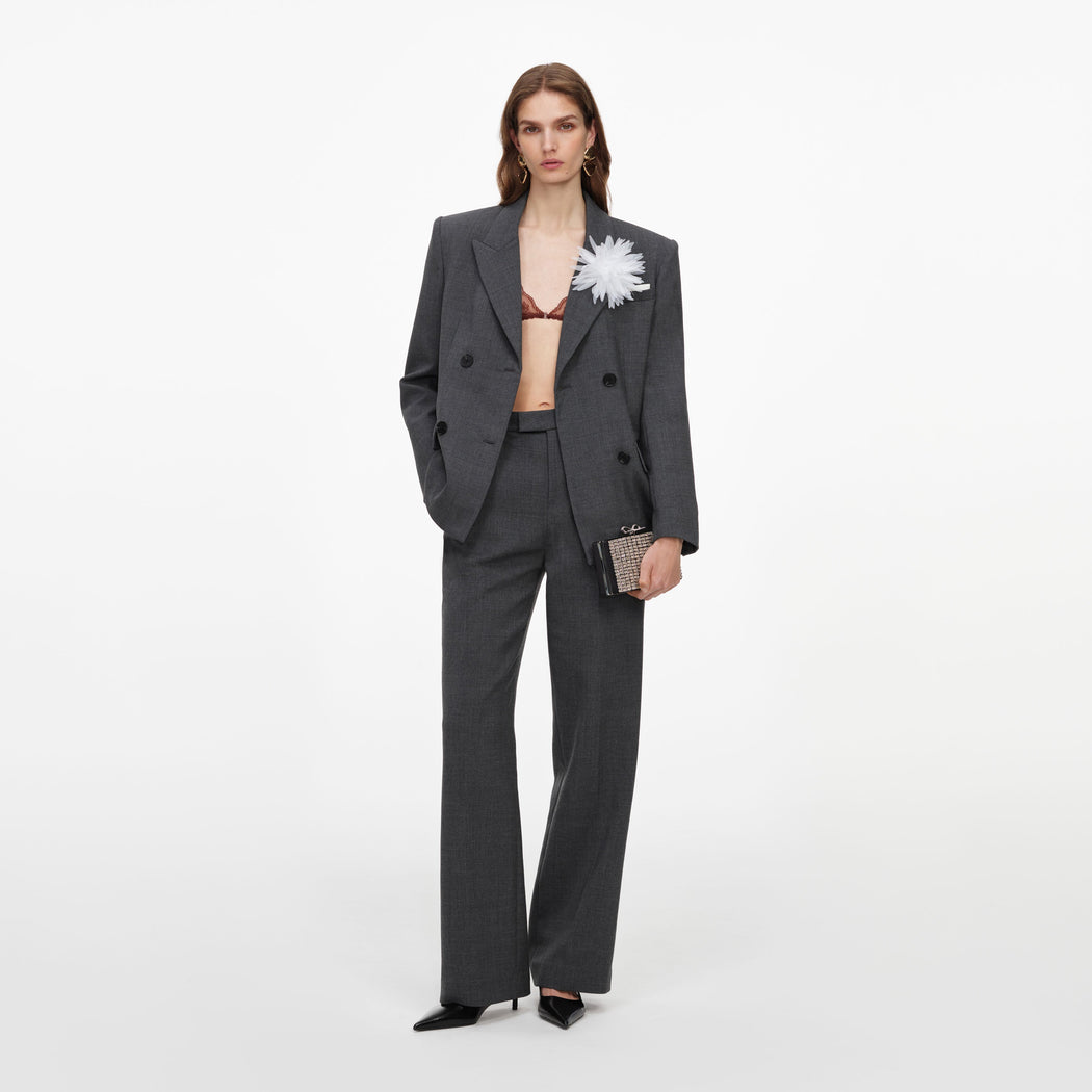 Woman in a dark grey suit with a white flower brooch, holding a small embellished clutch