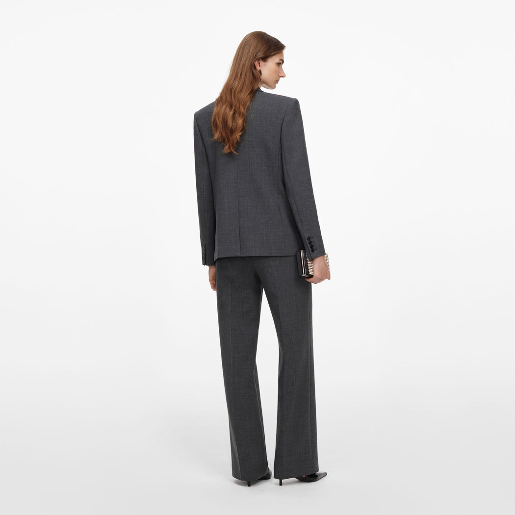 Woman in a dark grey suit, with a blazer and wide-leg trousers, holding a small clutch bag