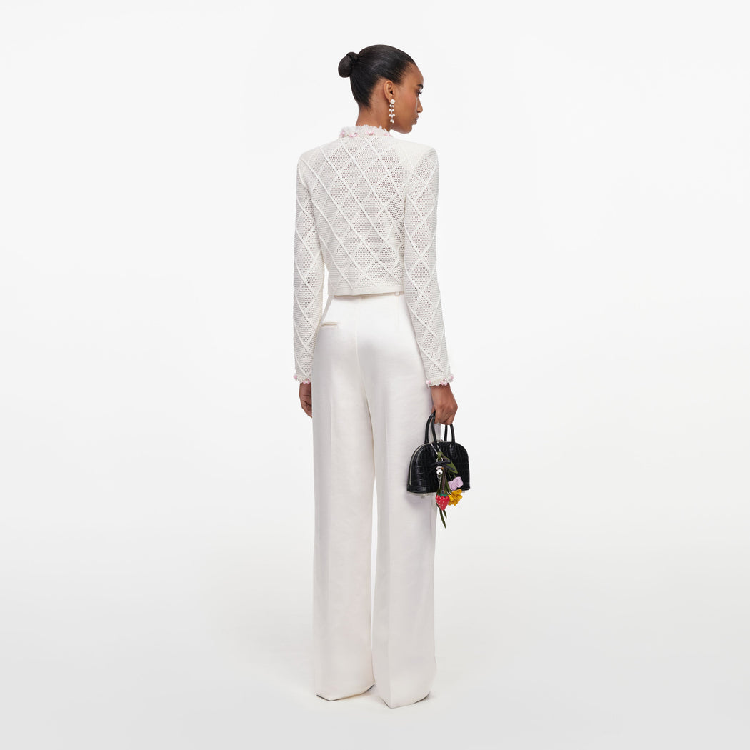 Woman in white crochet jacket and white trousers, holding a black handbag with floral charms