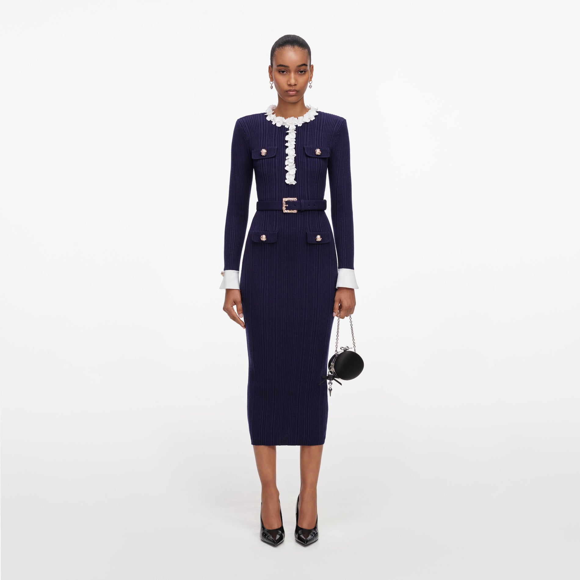Woman in a navy blue ribbed knit midi dress with white ruffled collar and cuffs, a matching belt, and black heels