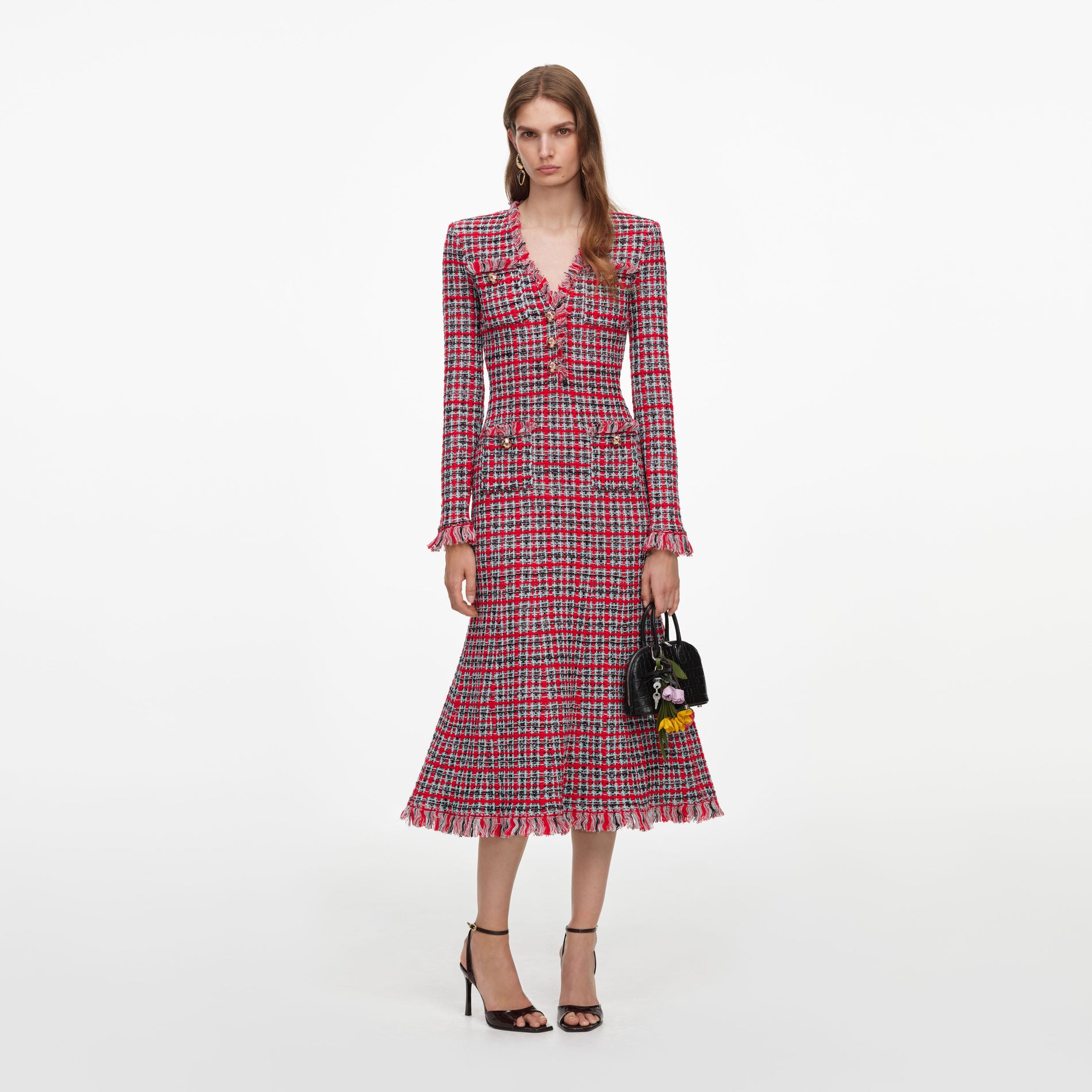 Woman in a red, black, and white plaid dress with fringe trim, holding a black handbag with flower charms