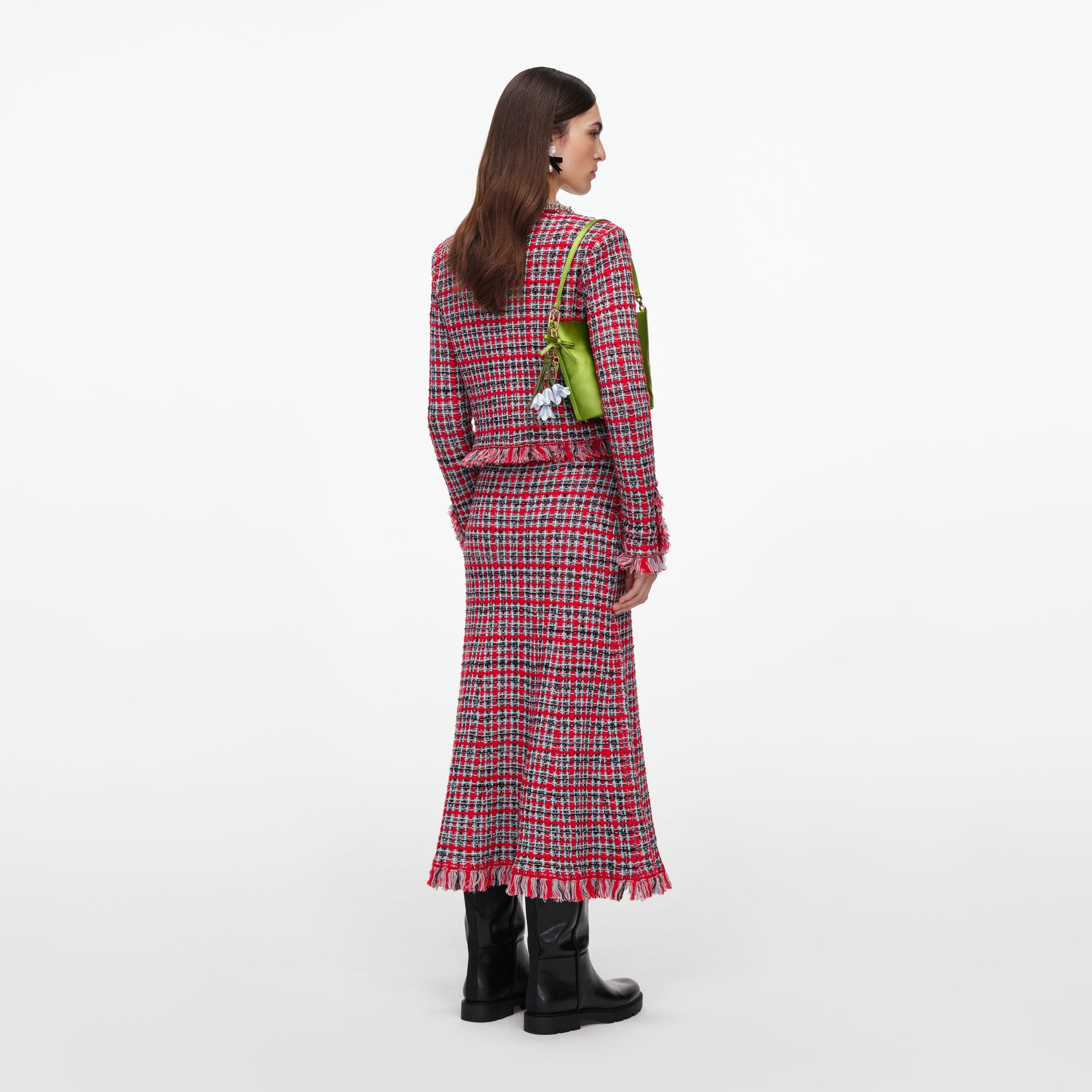Woman in red and black plaid tweed jacket and matching skirt with black boots and green handbag