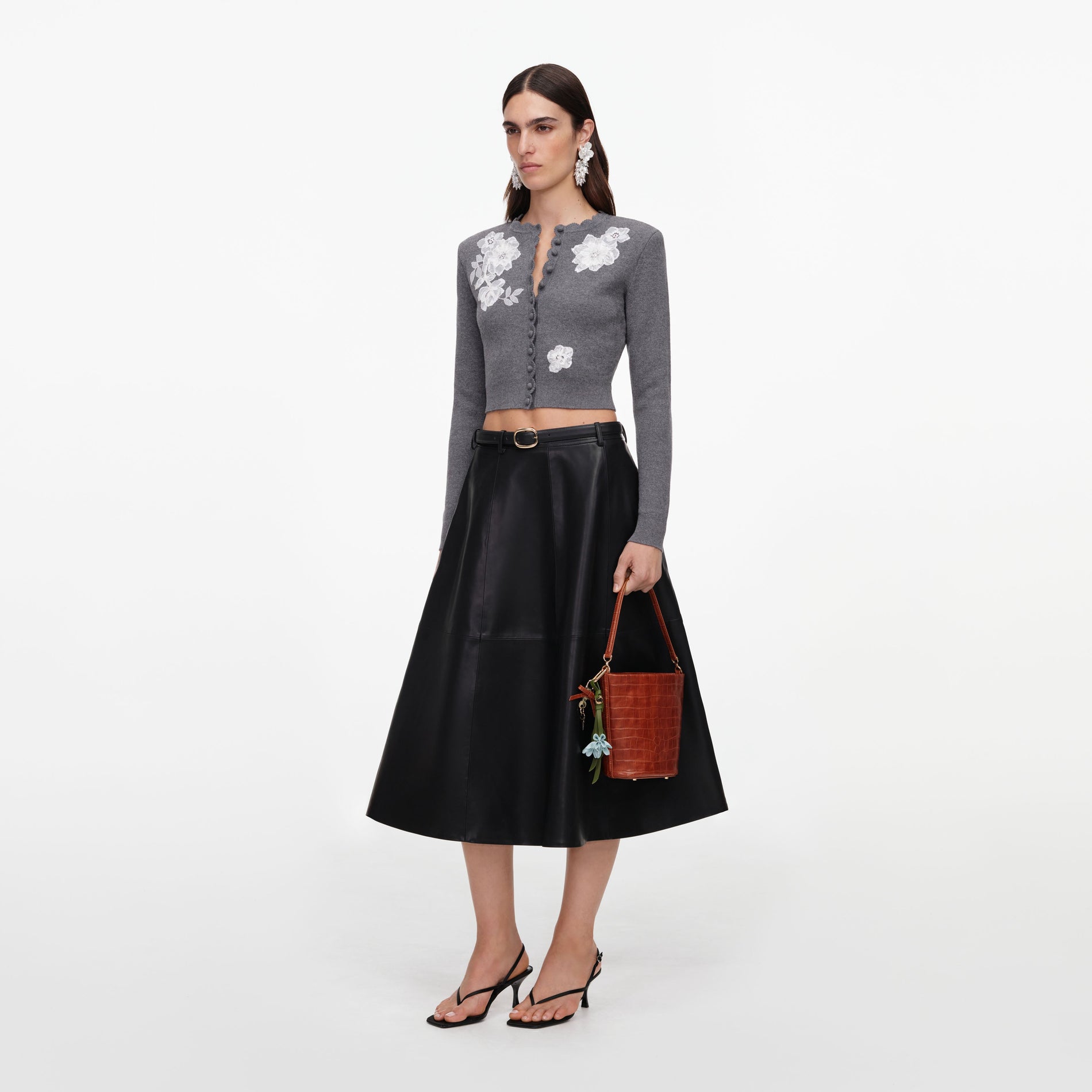 Woman in a grey cardigan with white floral embroidery, black leather midi skirt, and black heeled sandals