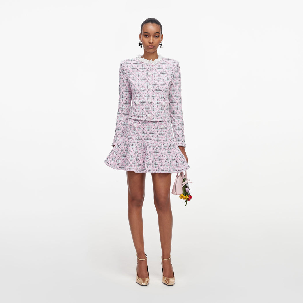 Woman in pink tweed jacket and matching skirt, holding a small pink handbag with flower charms
