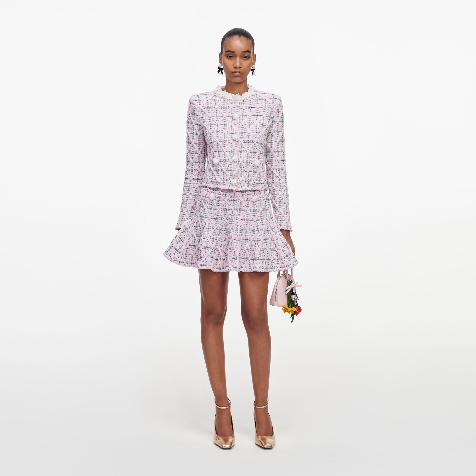 Woman in pink tweed jacket and matching skirt, holding a small pink handbag with flower charms