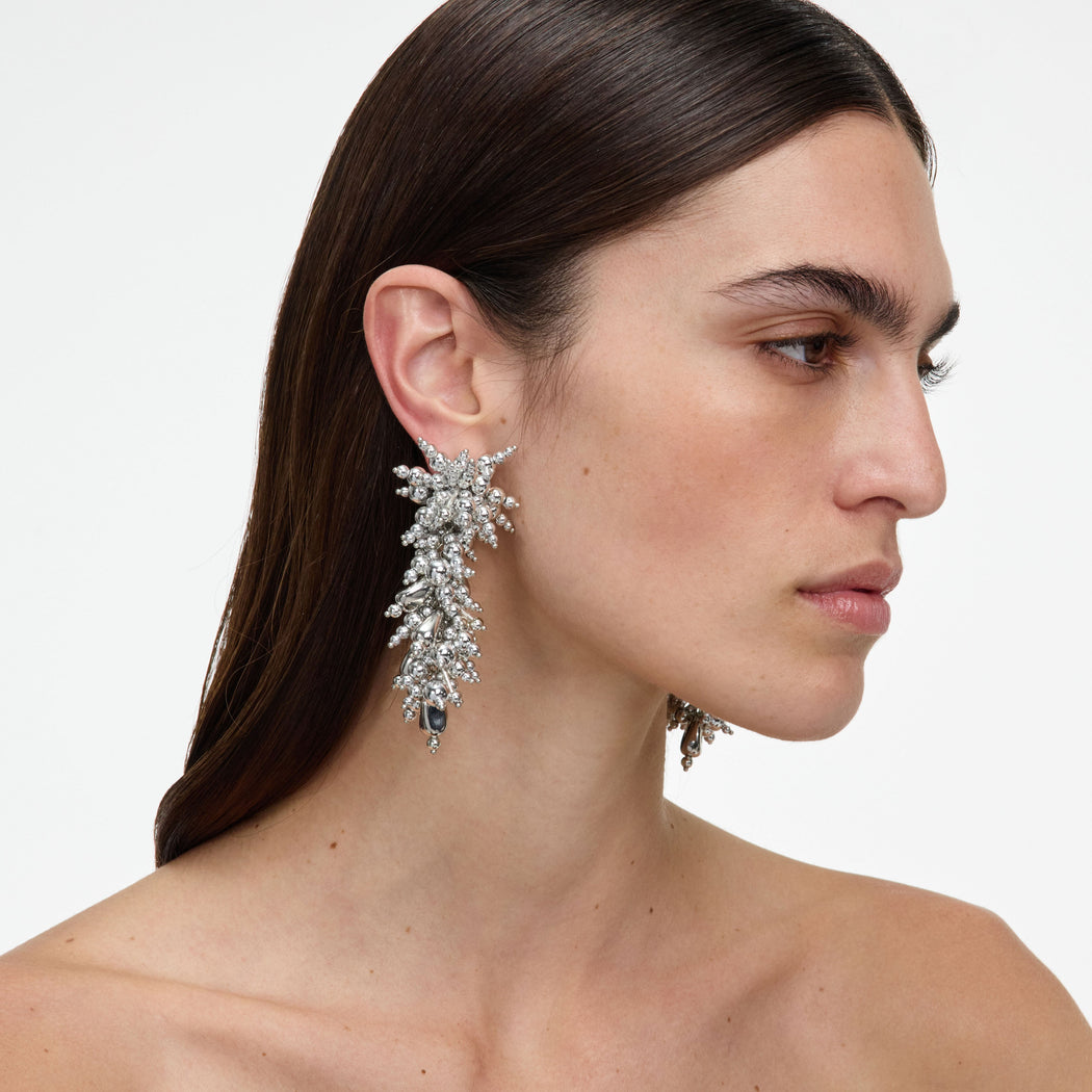Woman with dark hair wearing large, ornate silver earrings with multiple small and large spheres