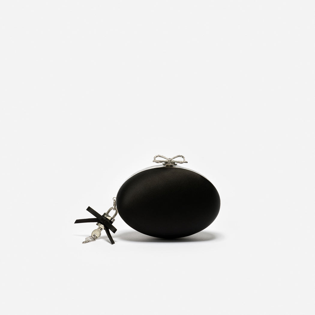 Black oval clutch bag with a silver bow clasp and a black ribbon and key charm