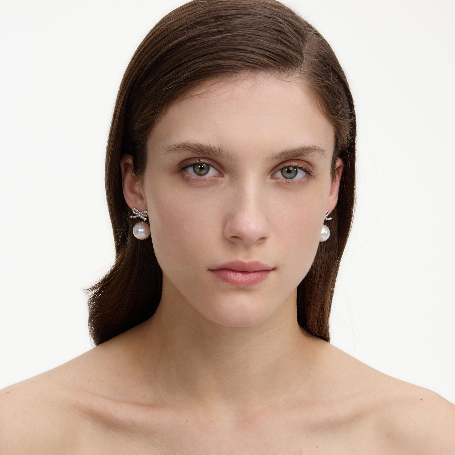 A close up of a woman wearing the Crystal Bow Pearl Back Earrings